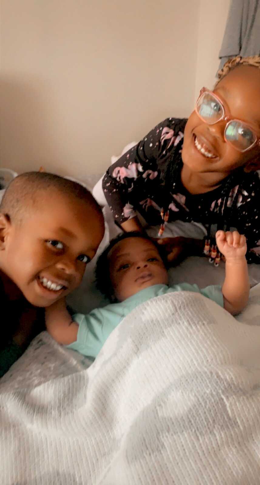 Older siblings smile while taking a photo with their newborn brother