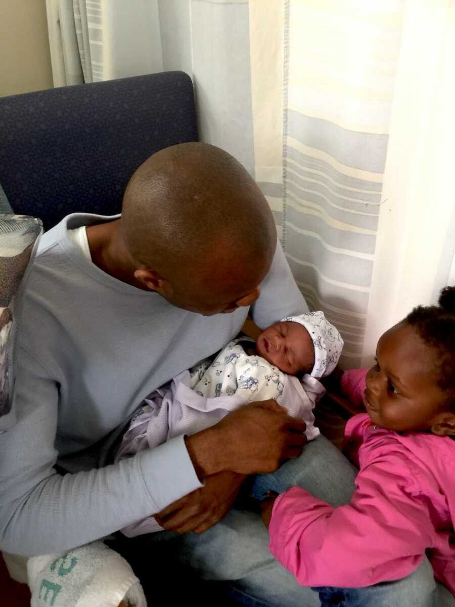 Dad holds his newborn child while introducing their older sibling to her