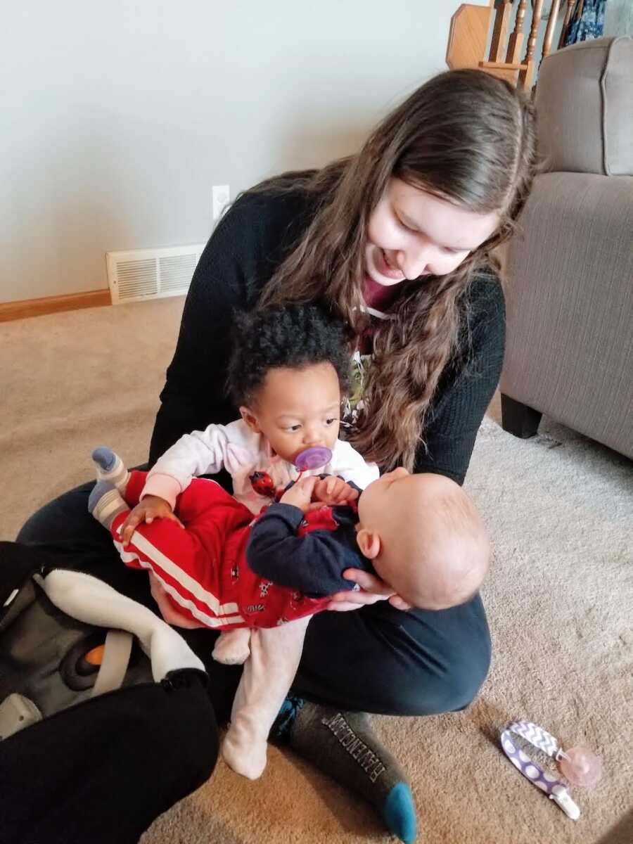 young woman holding two children she cares for to help moms