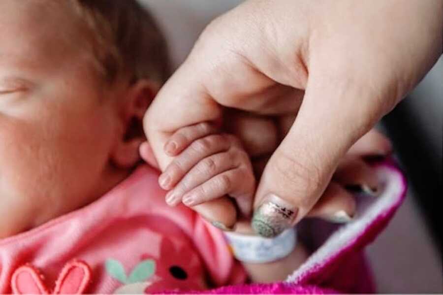 woman holds the small hand of a young baby