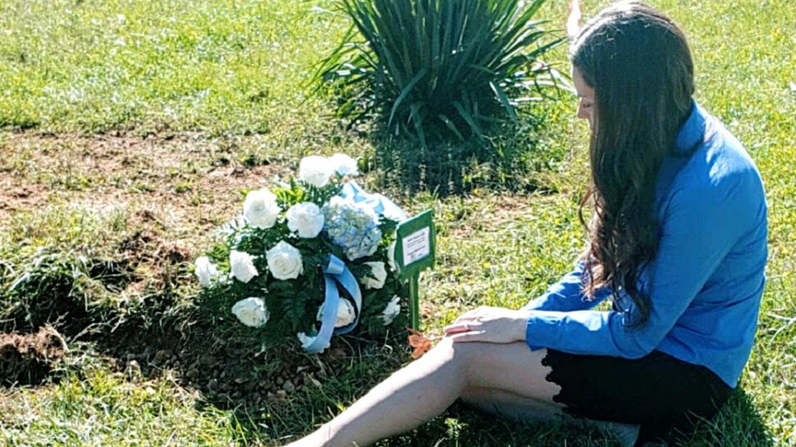 A woman sits with a bouquet of white flowers at her son's grave