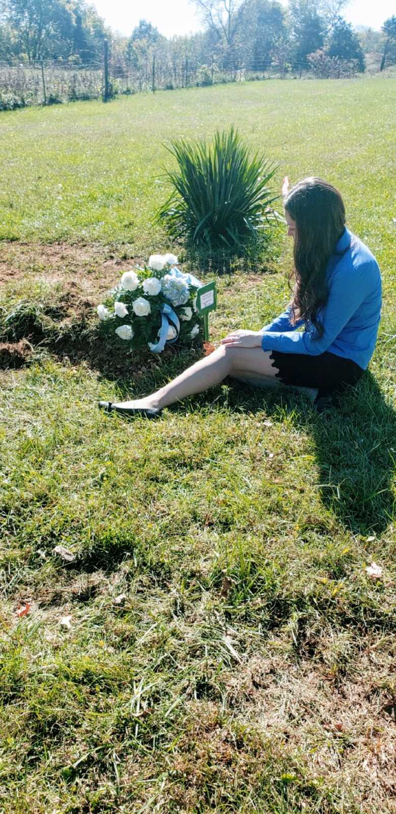 A woman sits with a bouquet of white flowers at her son's grave