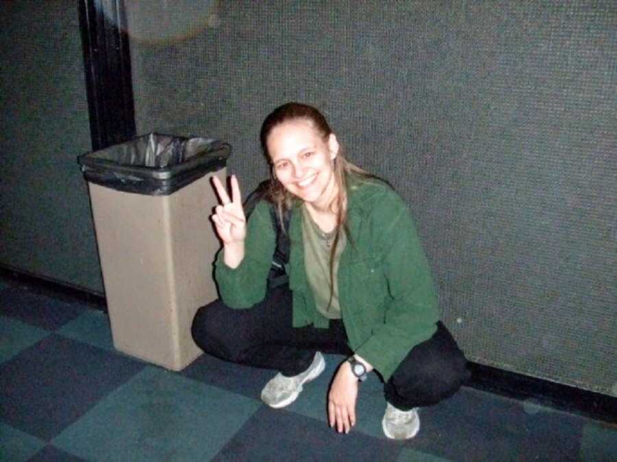 A woman with CRPS crouching wearing a green shirt and giving a peace sign