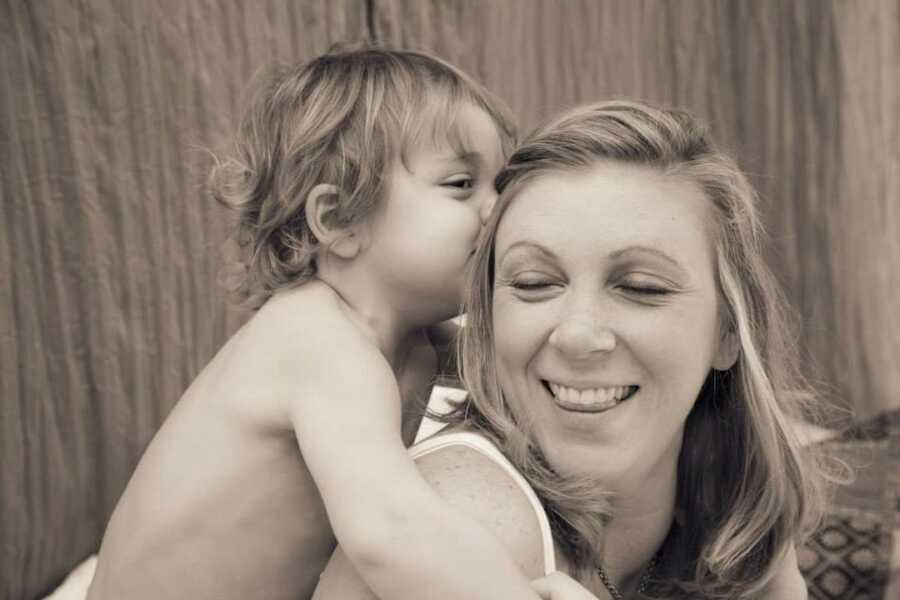 son stands behind his mother and gives her a kiss on the head