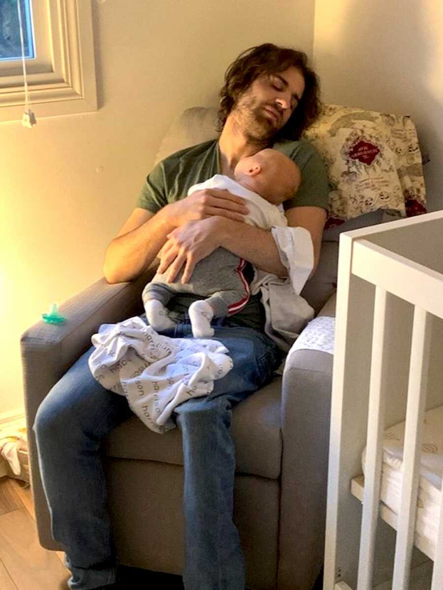 Father sits in a chair sleeping with his sleeping child on his chest