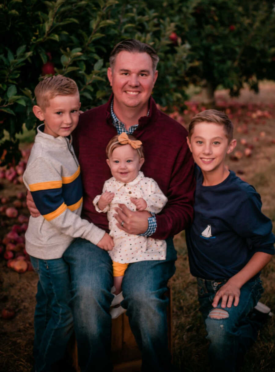 Father sits surrounded by his three children