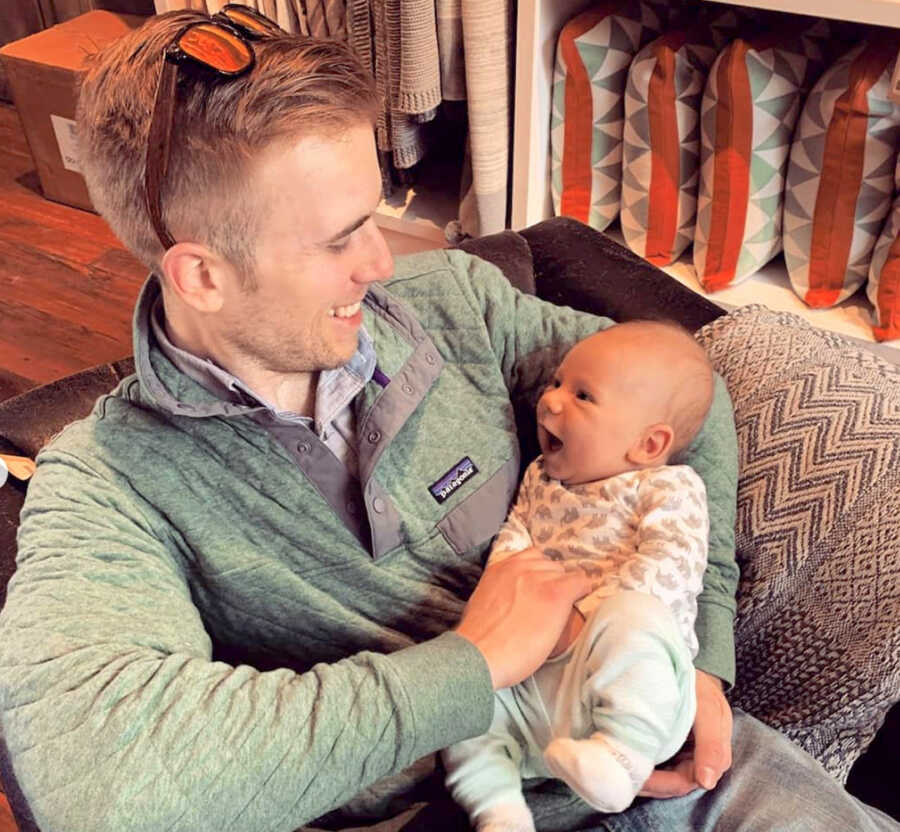 Father sits with his child in his arms, both are smiling