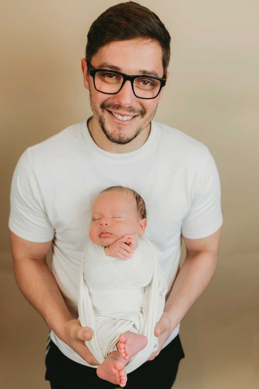 father stands smiling holding his newborn child