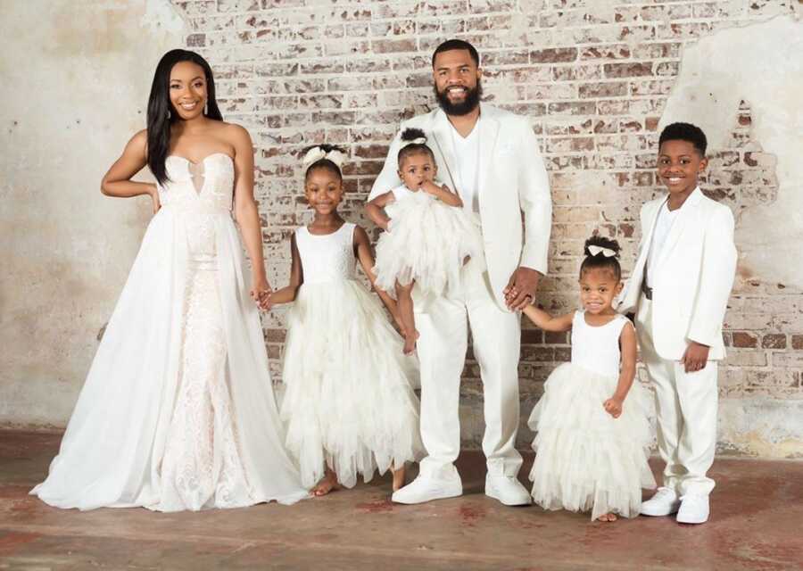 Couple stands together with their four children, all wearing white