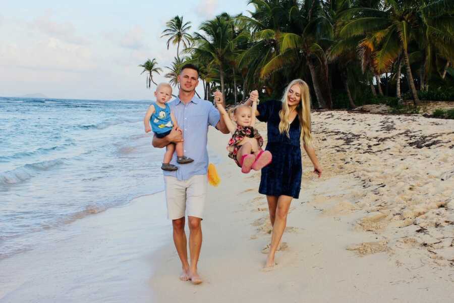 husband and wife walk along the beach with their two children