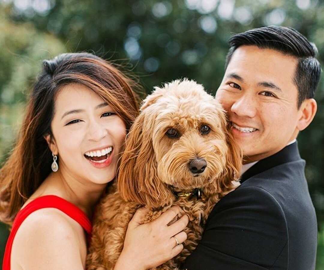 couple stands together holding their dog smiling