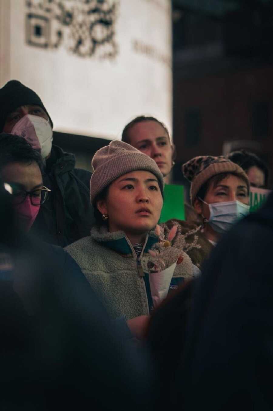 A woman stands in a crowd at a vigil after a mass shooting holding a bouquet of flowers