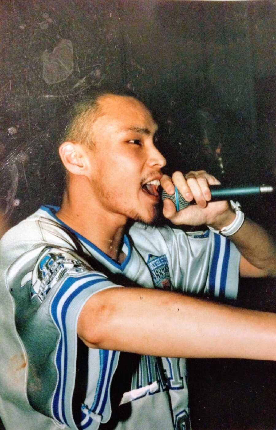 A man wearing a white and blue sports jersey singing into a microphone