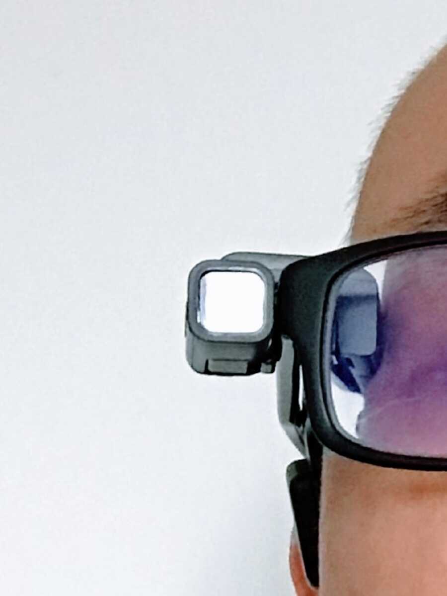 The side of a man's glasses equipped with a piece of assistive technology