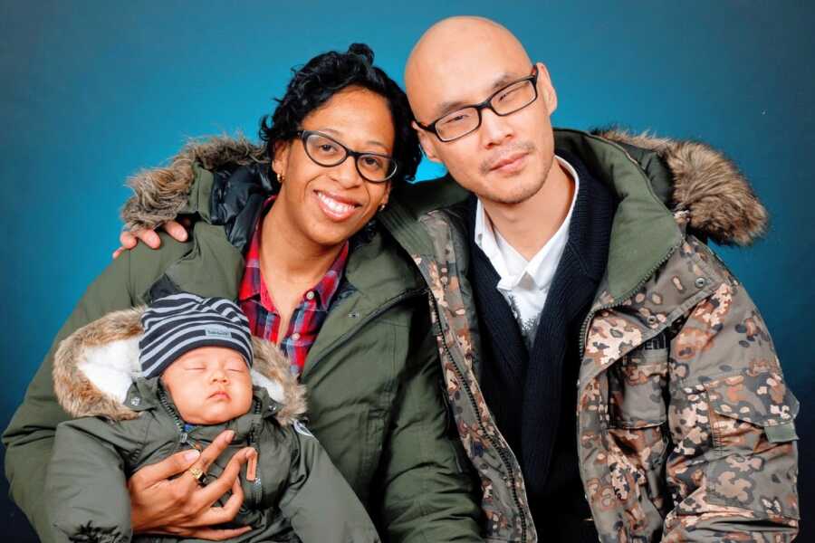 A man sits with his wife and his newborn baby all three wearing green jackets