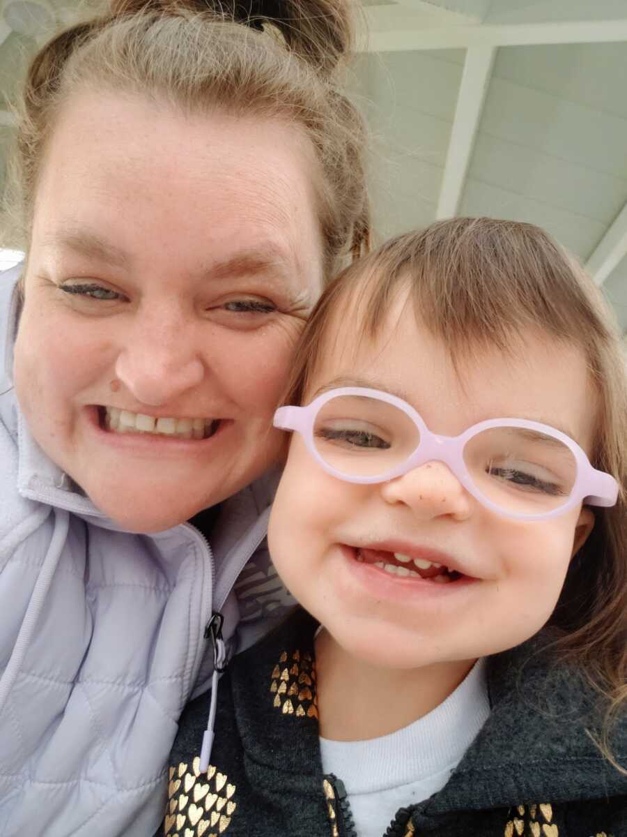 A mom holds her young autistic daughter wearing pink glasses