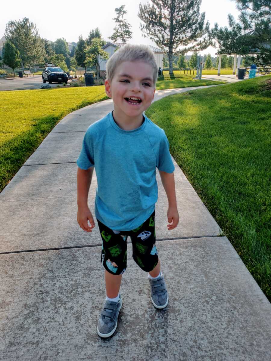 A little boy wearing a blue shirt and standing on a sidewalk outside