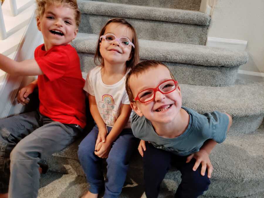 Three autistic siblings sit on grey carpeted stairs