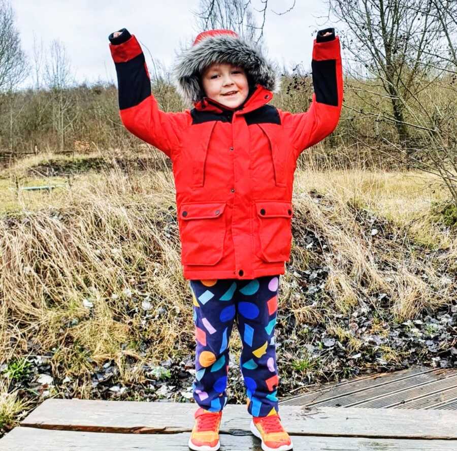 A young autistic boy wearing a red jacket and colorful pants