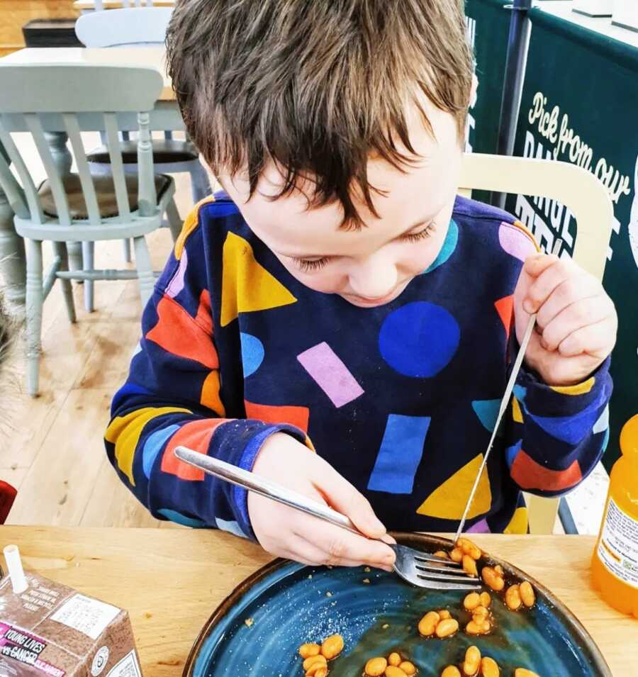 A boy wearing a colorful shirt eats beans