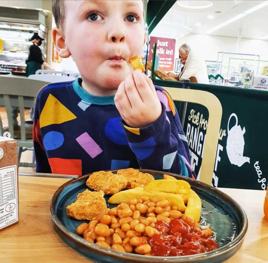 A boy eating chicken, fries, and beans off of his plate