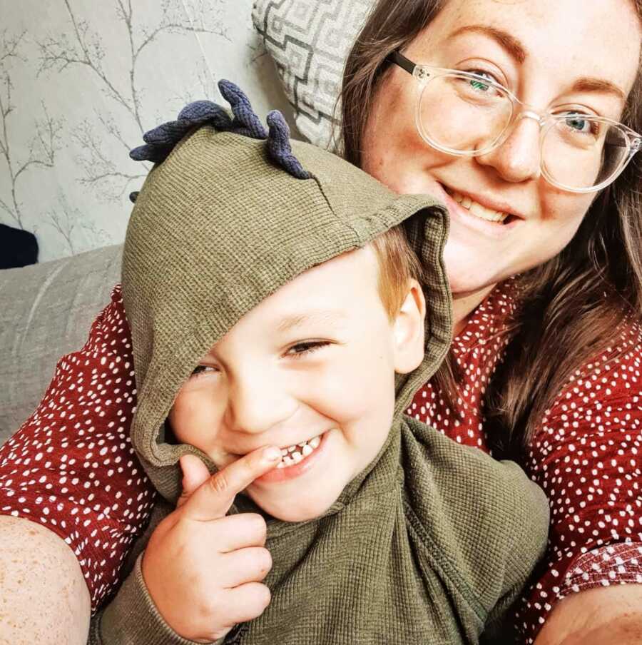 A mom holds her autistic son who is wearing a dinosaur hoodie
