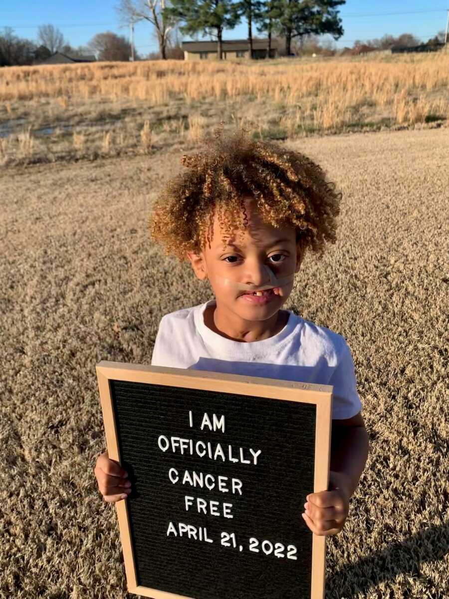 boy holding up sign saying he is cancer free