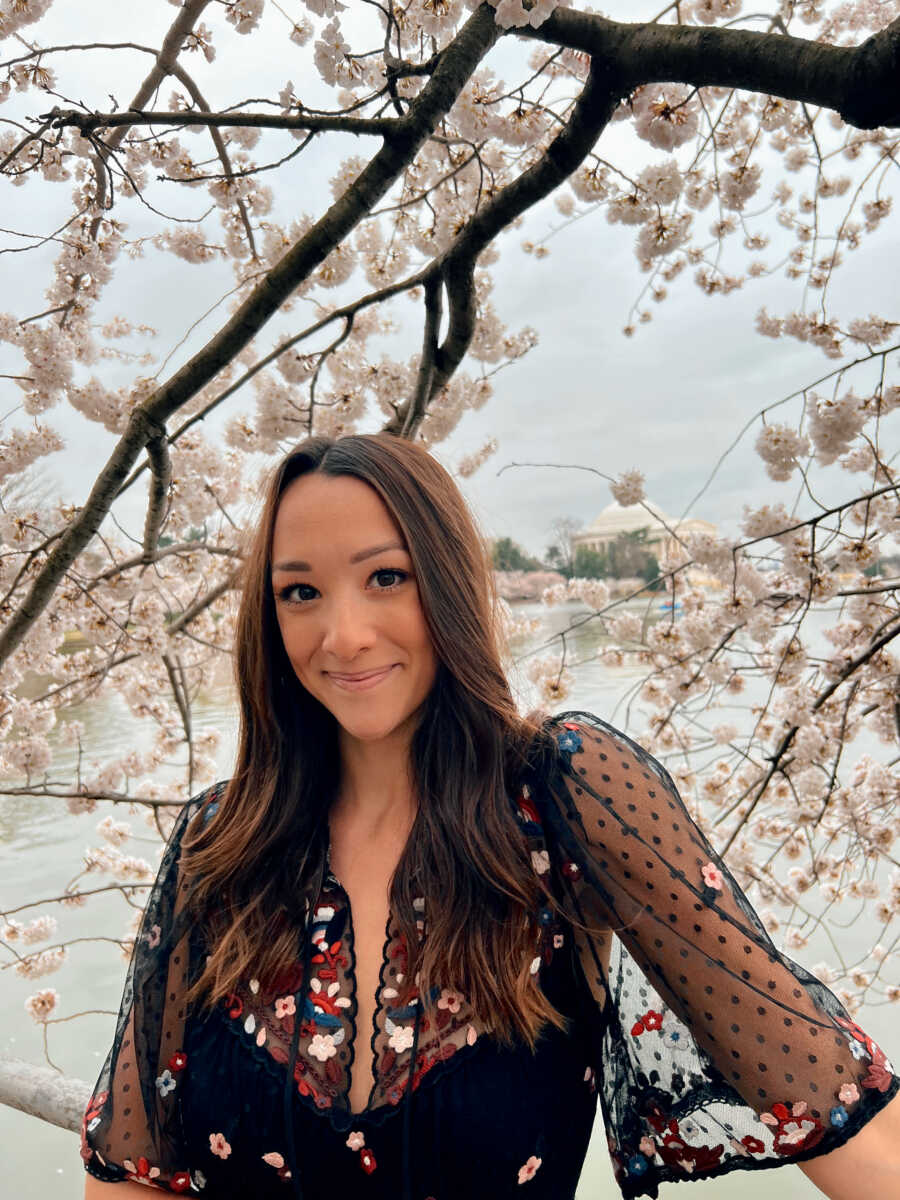 Former foster youth and adoptee stands in front of cherry blossom tree.