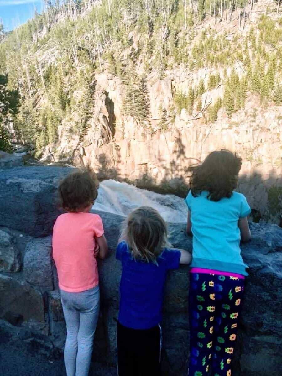 Three kids stand overlooking a river with a waterfall