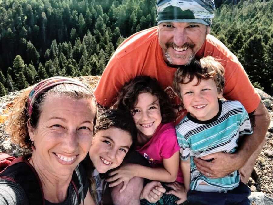 A family of five stand on a rock overlooking a large forest