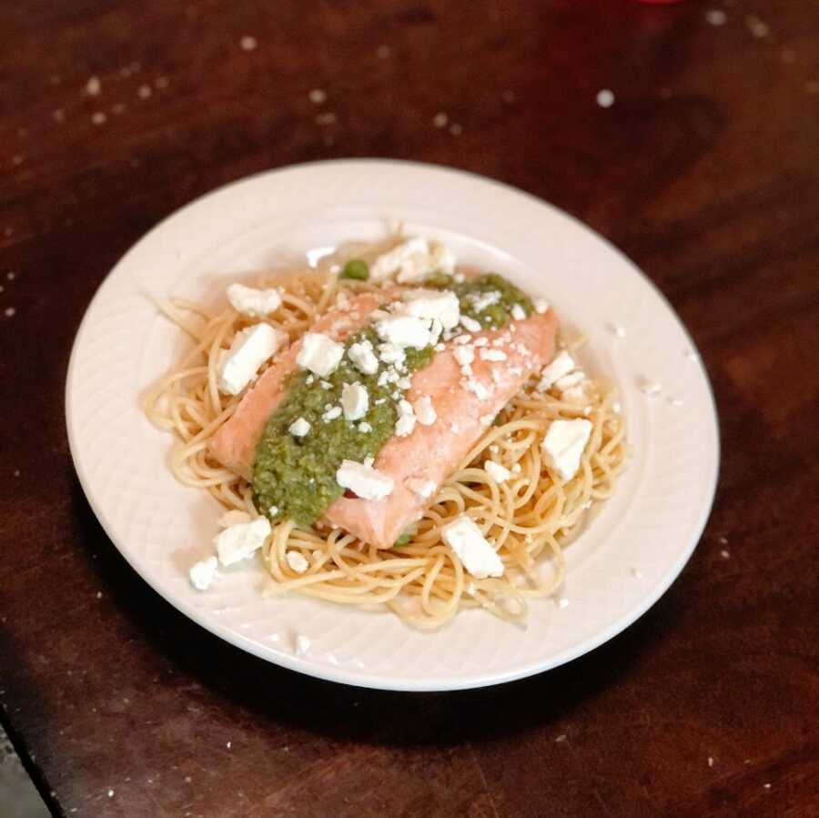 A bowl of pasta topped with salmon, cheese, and pesto