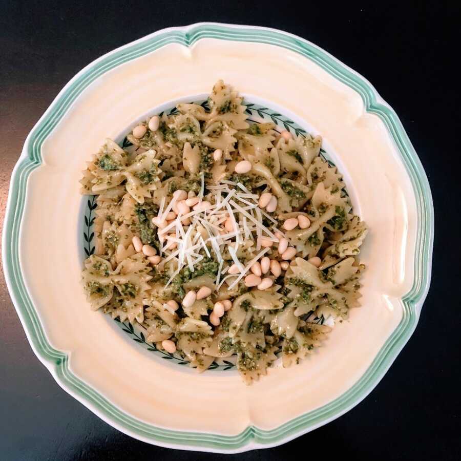 A bowl of pesto farfalle pasta topped with pine nuts and shredded cheese