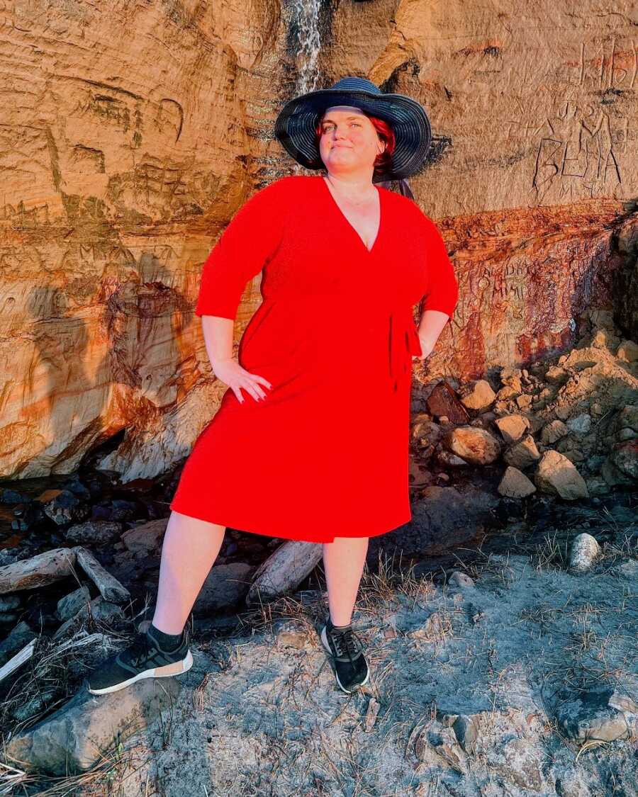 A woman wearing a red dress and a sun hat standing by some rocks