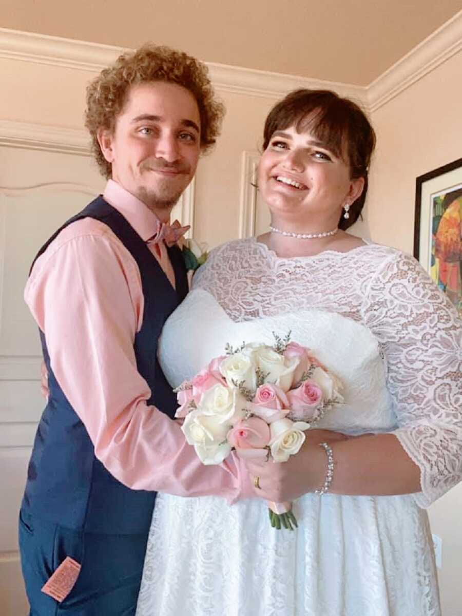 A bride and groom standing together on their wedding day holding a bouquet