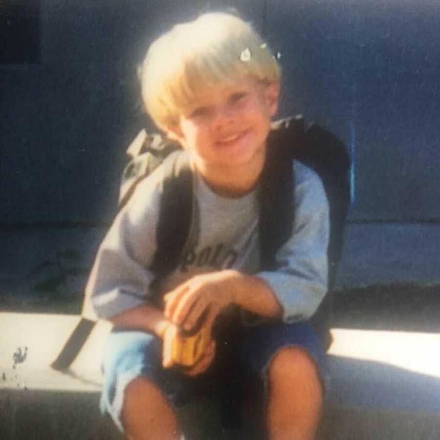 little brother sits on stairs with backpack ready for school