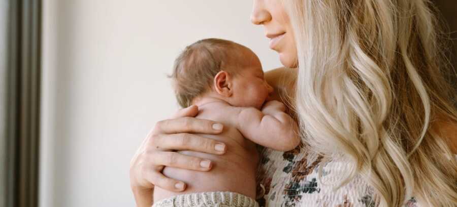 mom holds her newborn baby at her shoulder and looks down at them