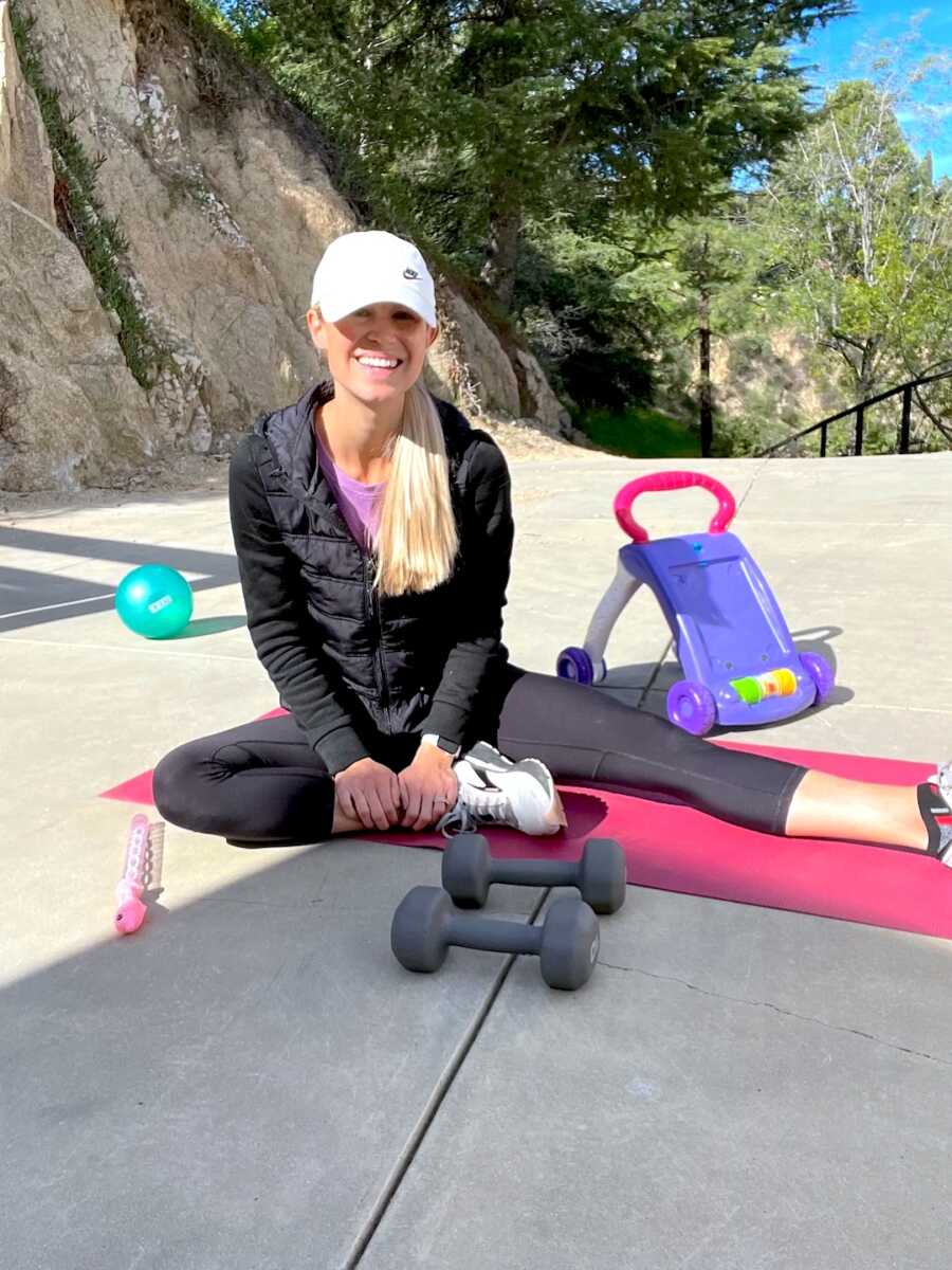 mom sits on yoga mat with children's toys around her