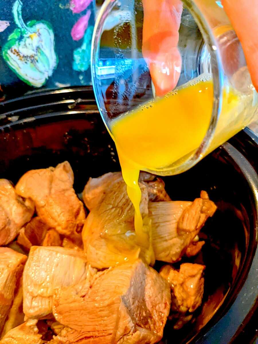 adding orange juice to the slow cooker with the pork