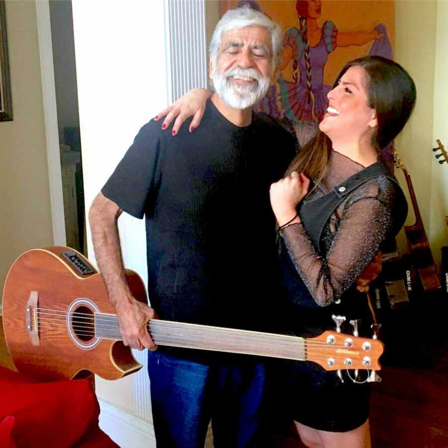 daughter looks lovingly at her father while he holds a guitar smiling
