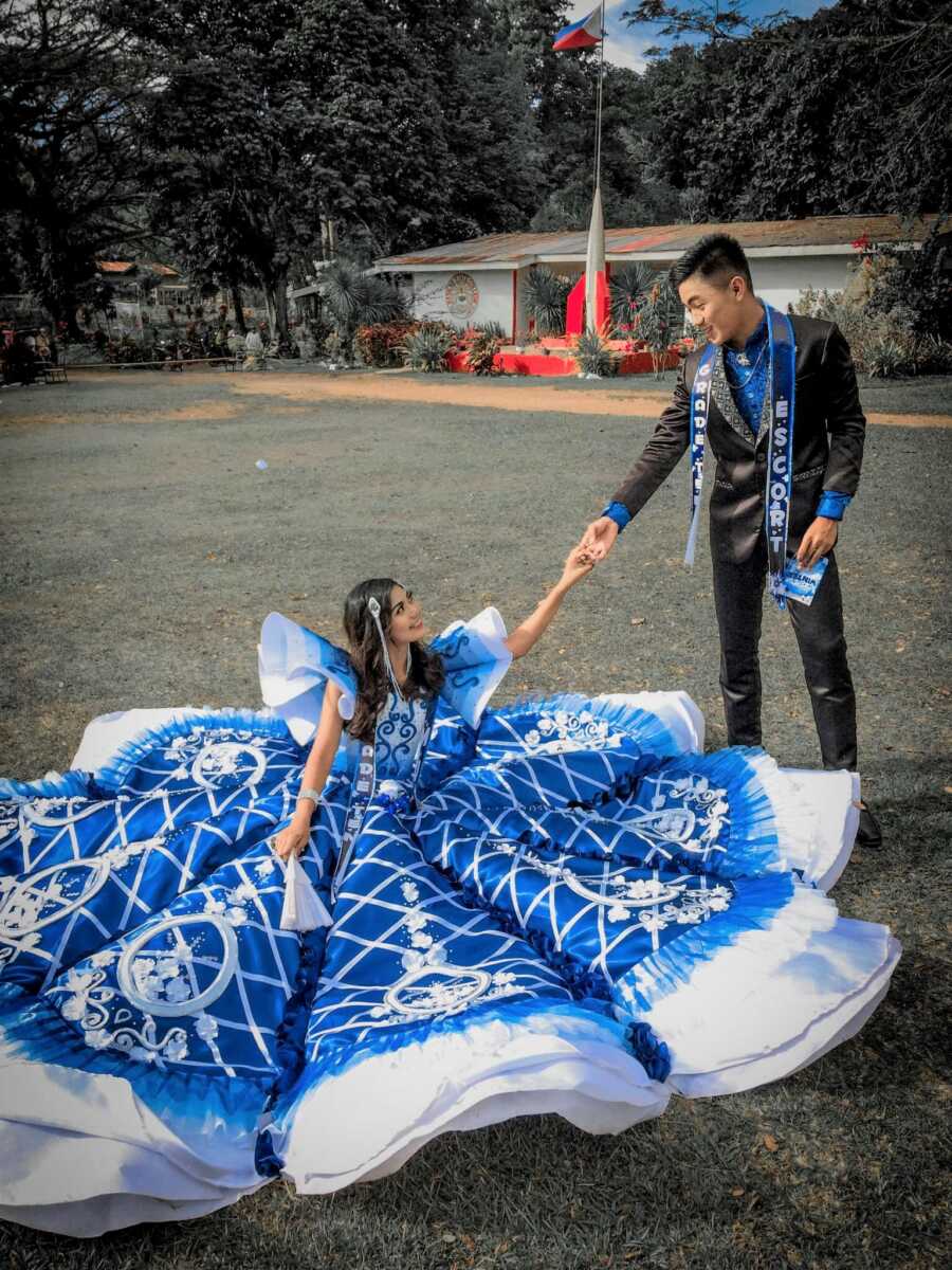 girl sits on the ground in her prom dress while her date holds her hand