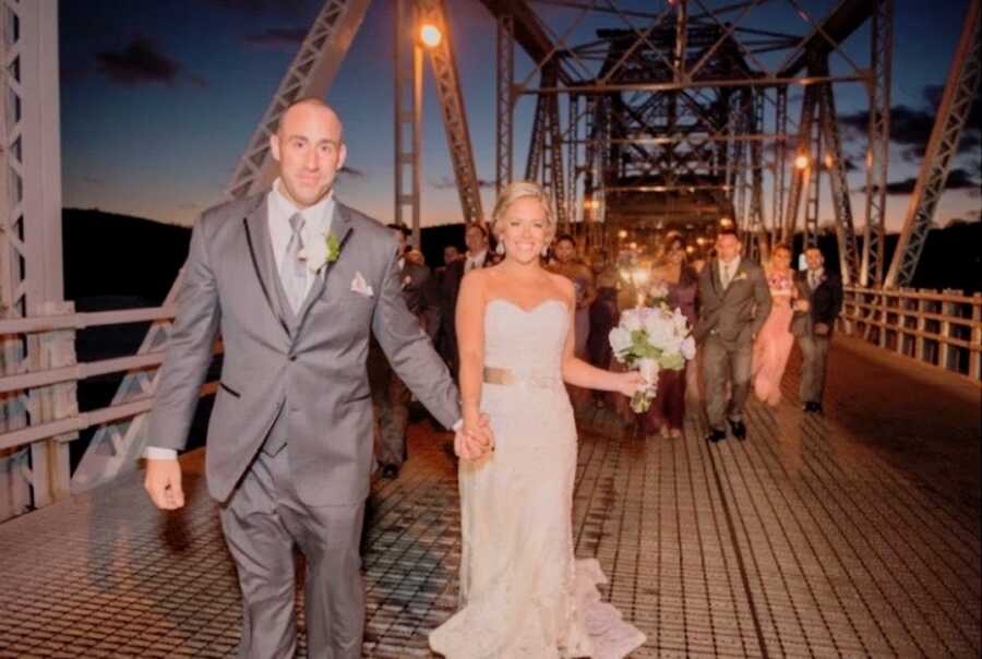 Husband and wife hold hands walking on their wedding day, their family behind them