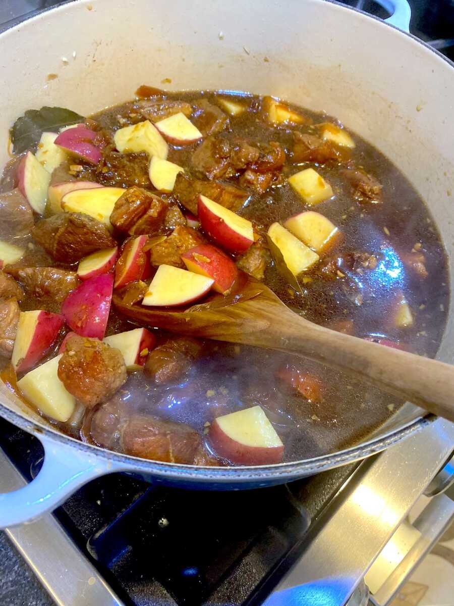 Adding red potatoes into the pot with adobo