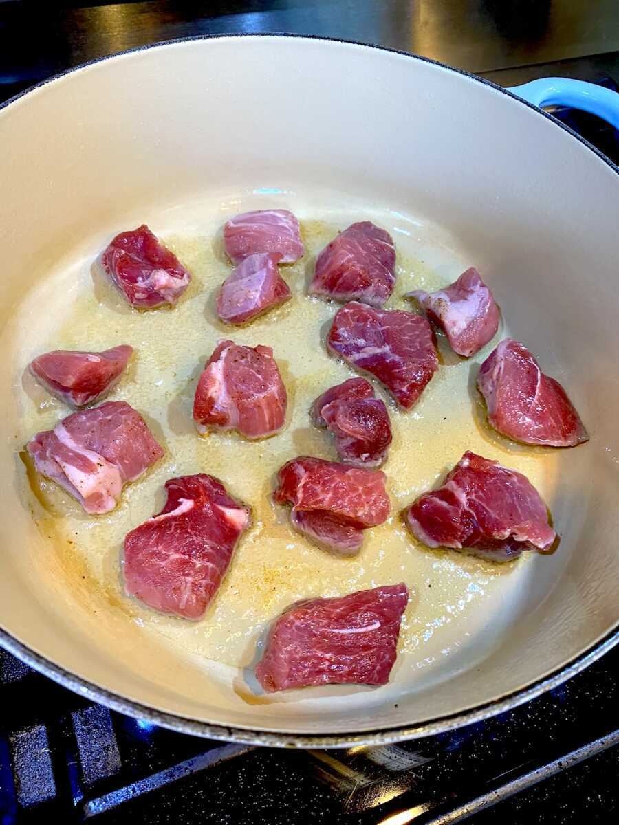 placing the pork pieces into pot with oil to brown