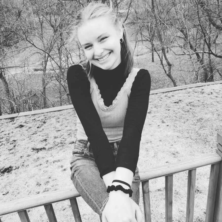 teenage girl sits on deck railing smiling