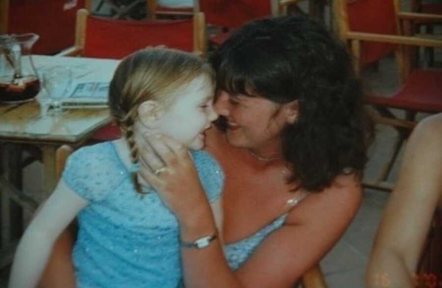 A mom sits with her daughter in her lap pressing noses together