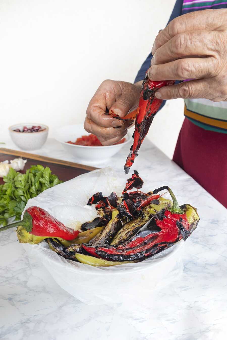 A grandmother peeling the charred skin off of cooked banana peppers