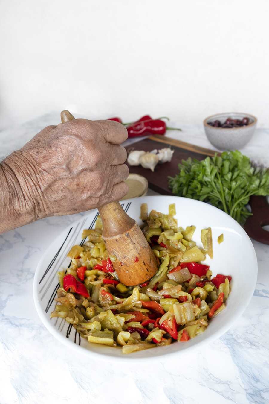 A grandma mashing peppers in a mortar with a pestle