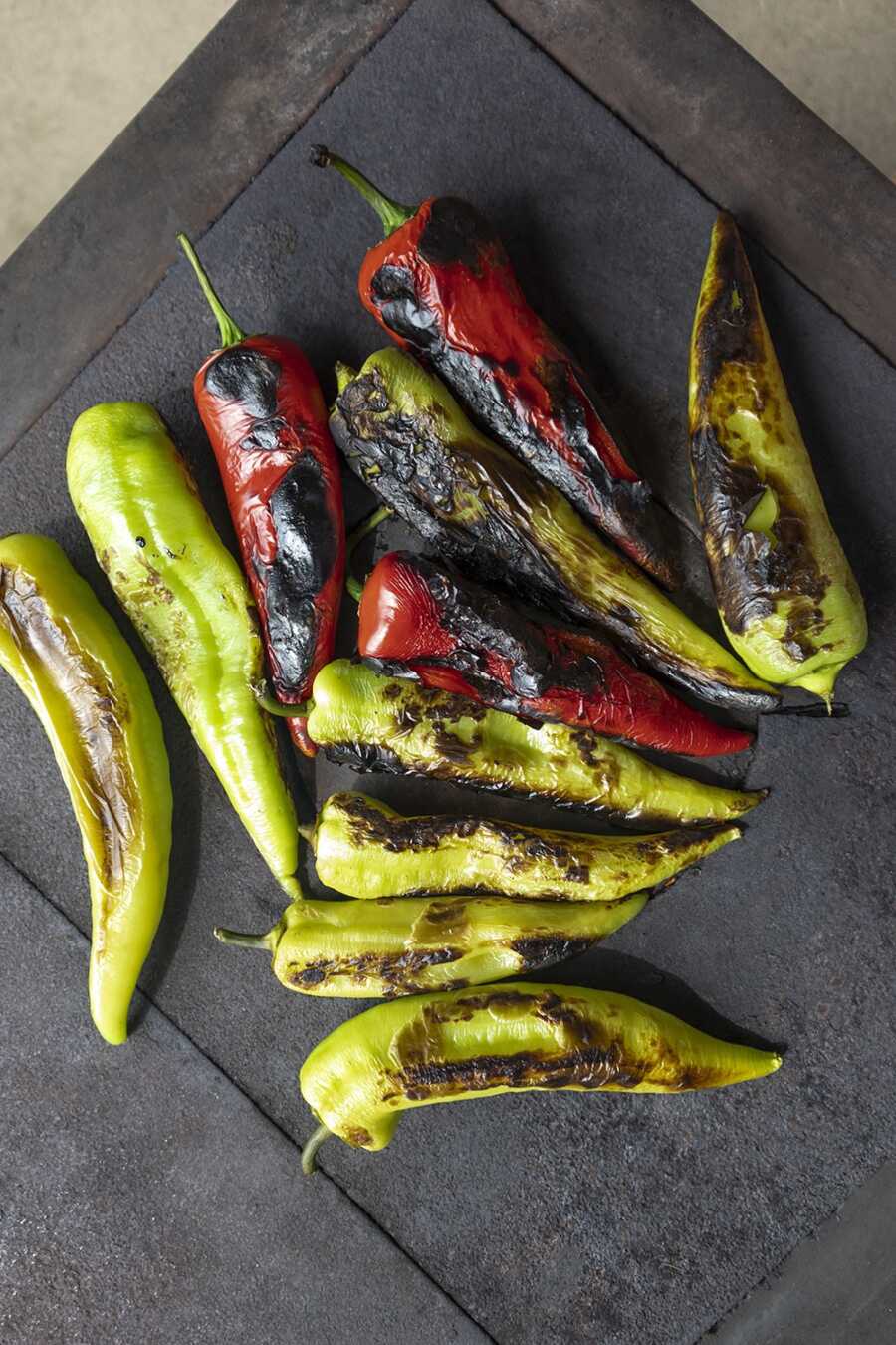 Green and red banana peppers charring on a grill
