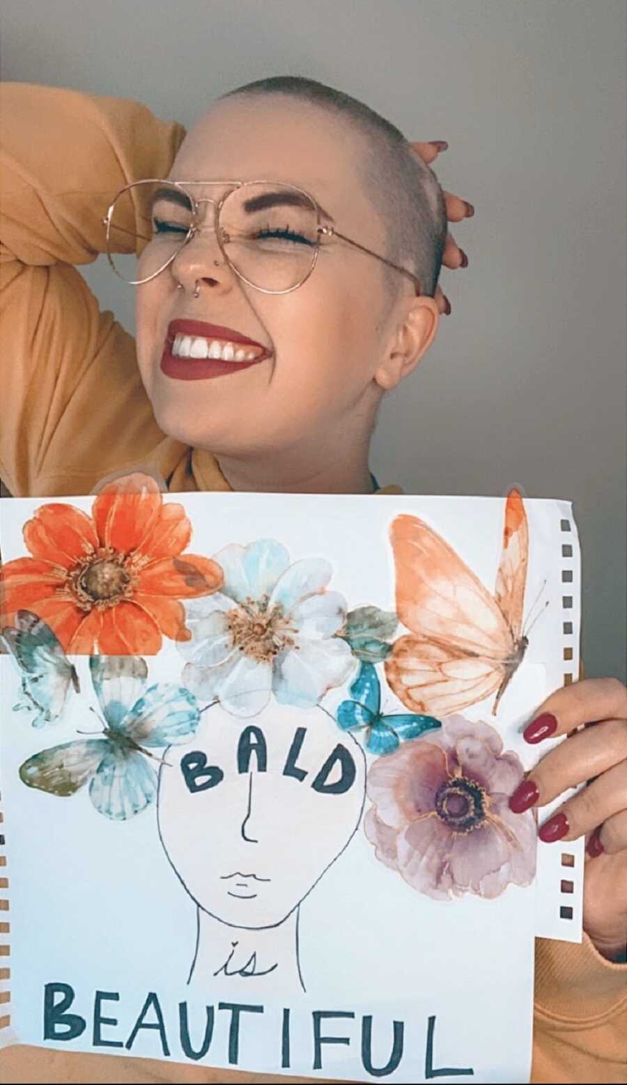 A woman wearing glasses holds up a sign to raise baldness awareness
