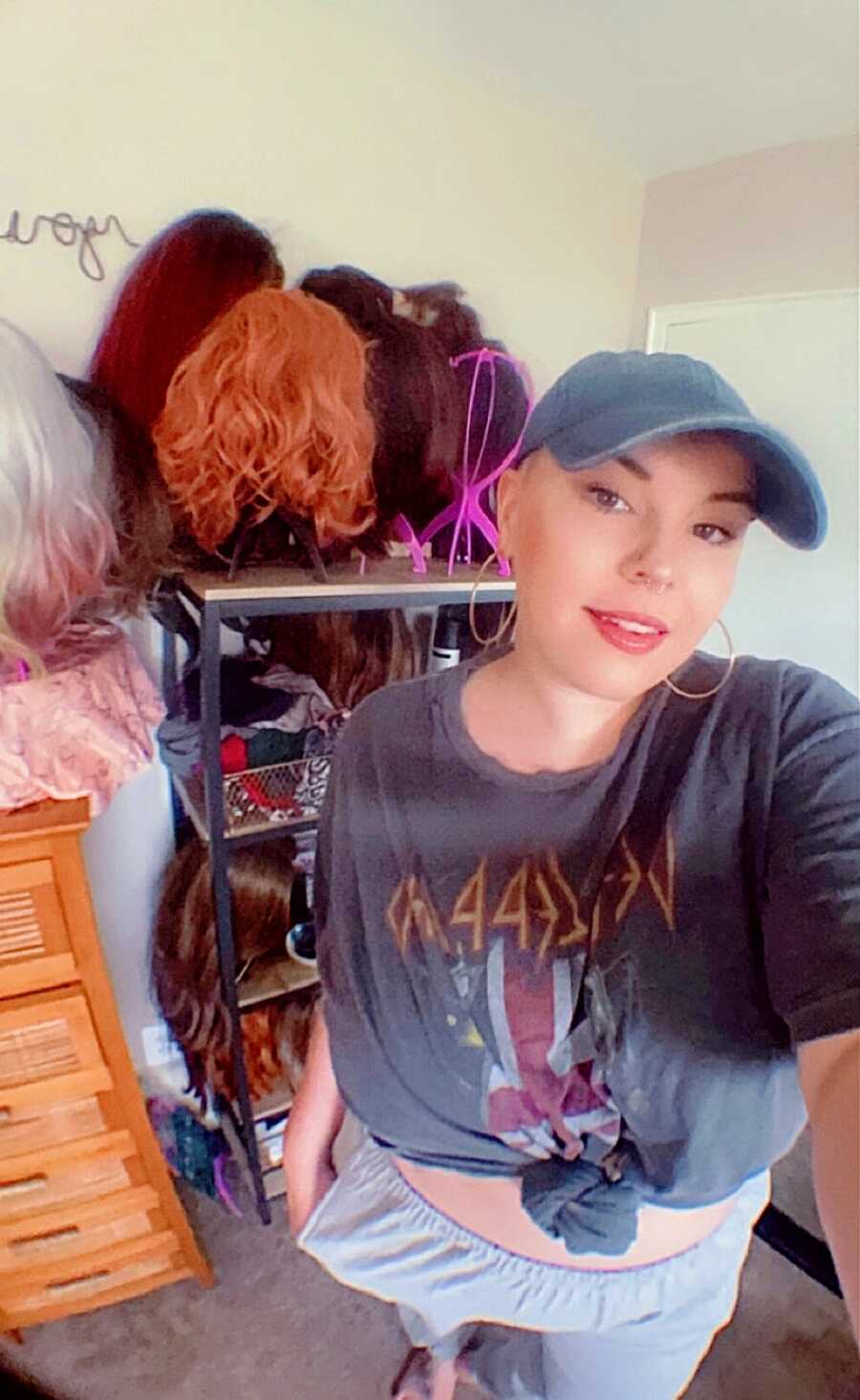 A woman wearing a baseball cap stands in front of her wigs